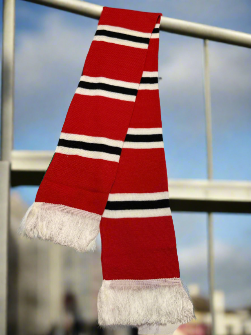 Red scarf with black and white stripes draped over a railing against a blurred outdoor background