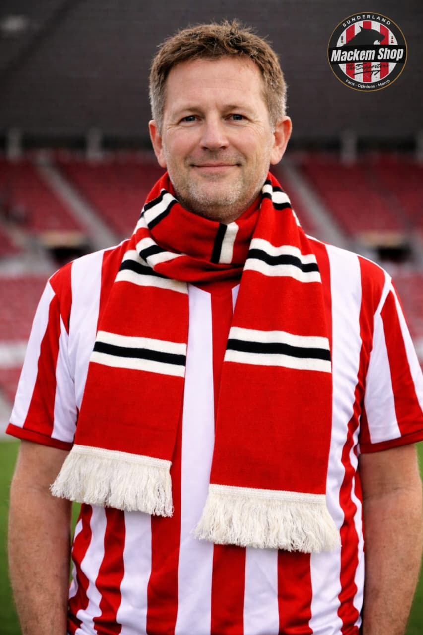 Man wearing a red and white striped scarf with fringes, standing on a sports field.