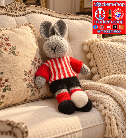 A red and white hand knitted Rabbit is on an off White Sofa, with a MackemShop logo is visible on top right corner.
