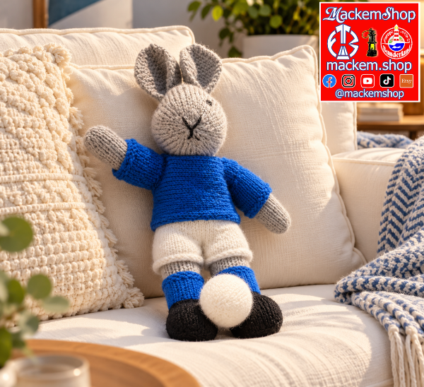 A hand Knitted Rabbit is on a white modern sofa with blue and white colours, A MackemShop logo is visible on top right corner.