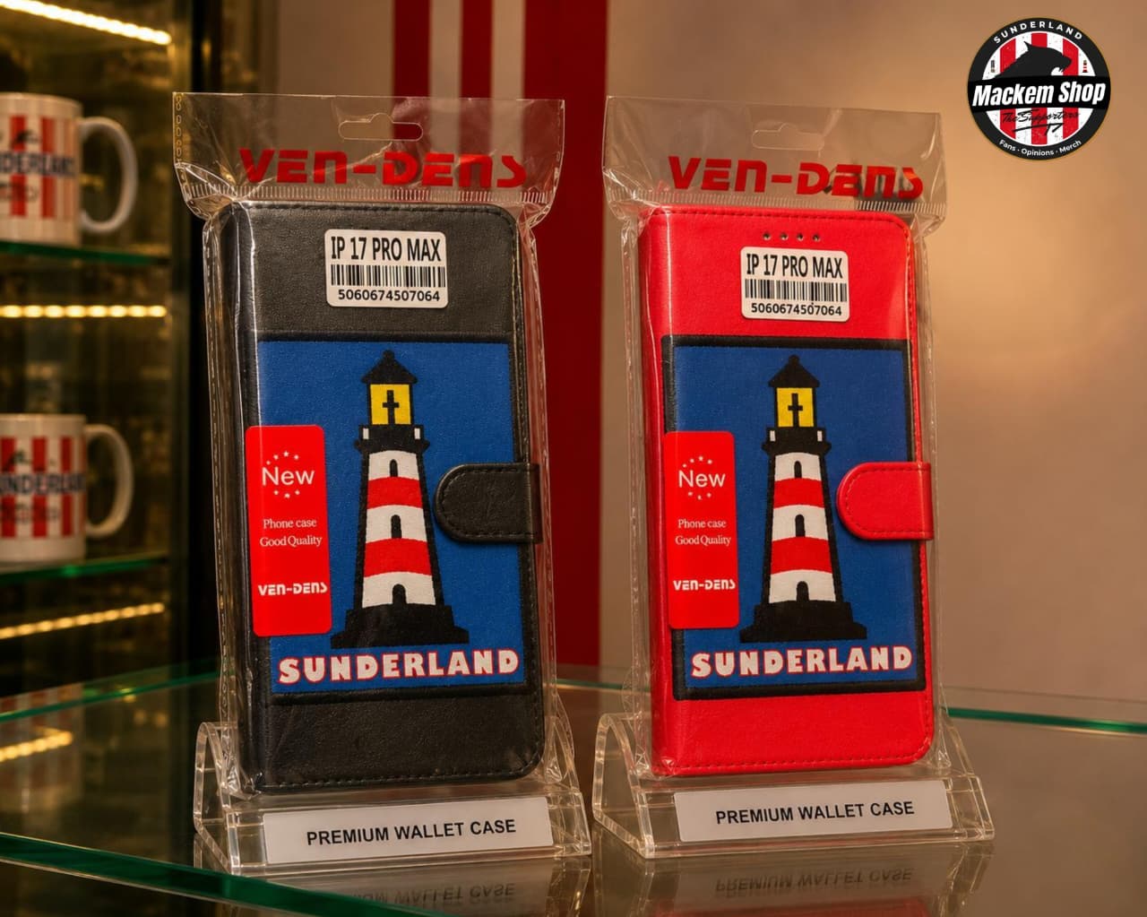 Two MackemShop product wallet cases in clear plastic packaging, displayed on a glass shelf. One case is black and the other is red, both featuring a blue front panel with a lighthouse graphic and the word 'SUNDERLAND'.