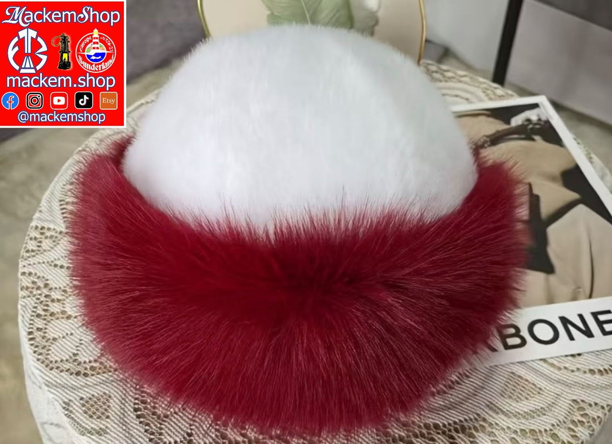 A plush fur hat with a white top section and a deep red lower band, displayed on a lace-covered surface with a magazine underneath. A prominent 'Mackemshop' logo overlay is visible in the top-left corner.