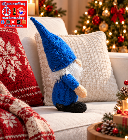 A knitted gonk sits on a white sofa in a cozy living room setting with a red patterned pillow, a knit blanket, and a decorated Christmas tree in the background. A 'MackemShop' logo overlay is visible in the top left corner.