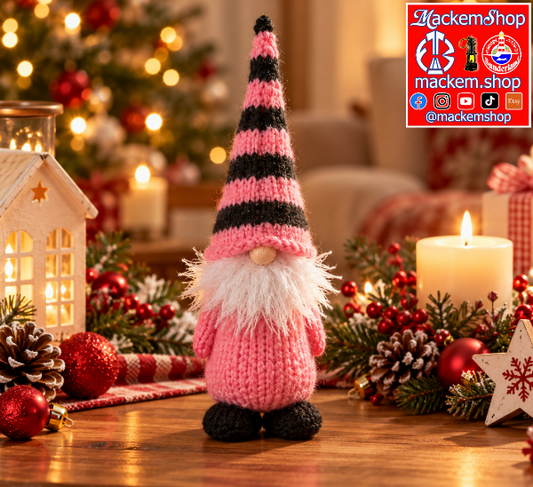 Pink and black knitted Christmas gonk, featuring a striped pointed hat, fluffy white beard, pink body and black feet, displayed on a wooden table with festive Christmas decorations, pinecones, red ornaments, candles and warm fairy lights.
A MackemShop Logo is Visible on top right corner.