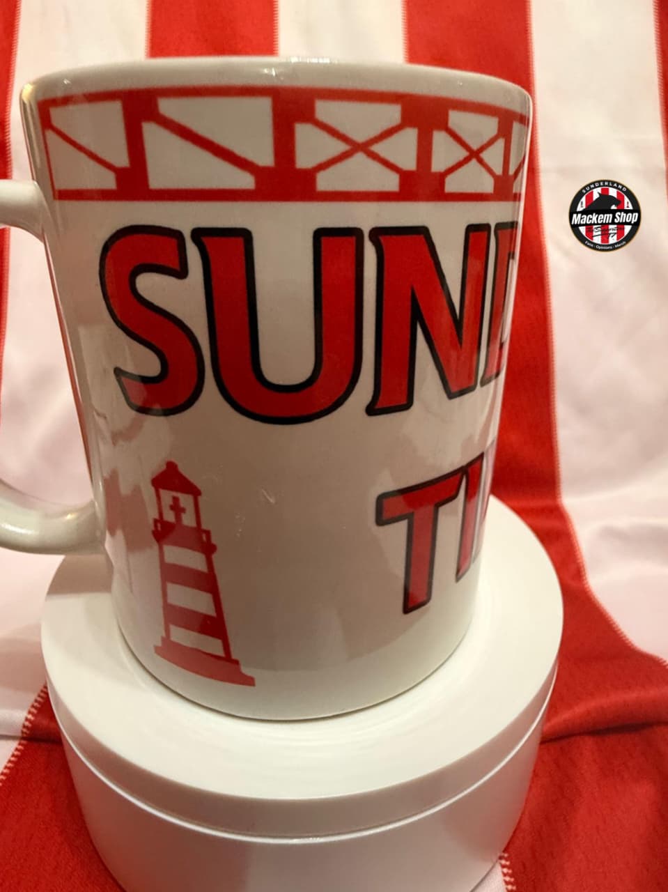 White mug with red and black text and graphics on a red and white striped background
