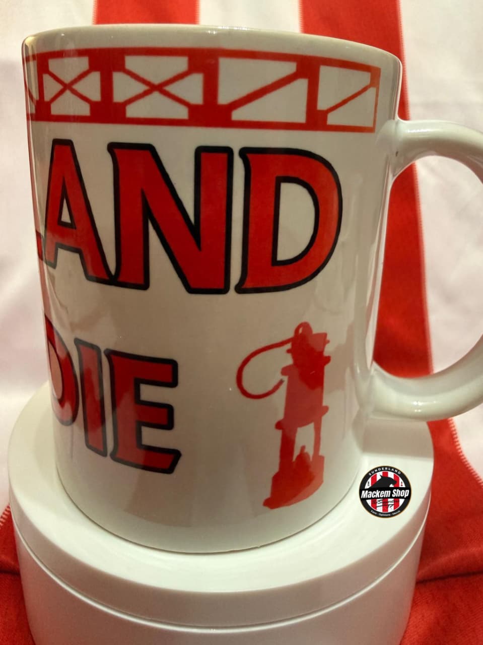 White mug with red and black text and graphics on a red and white striped background