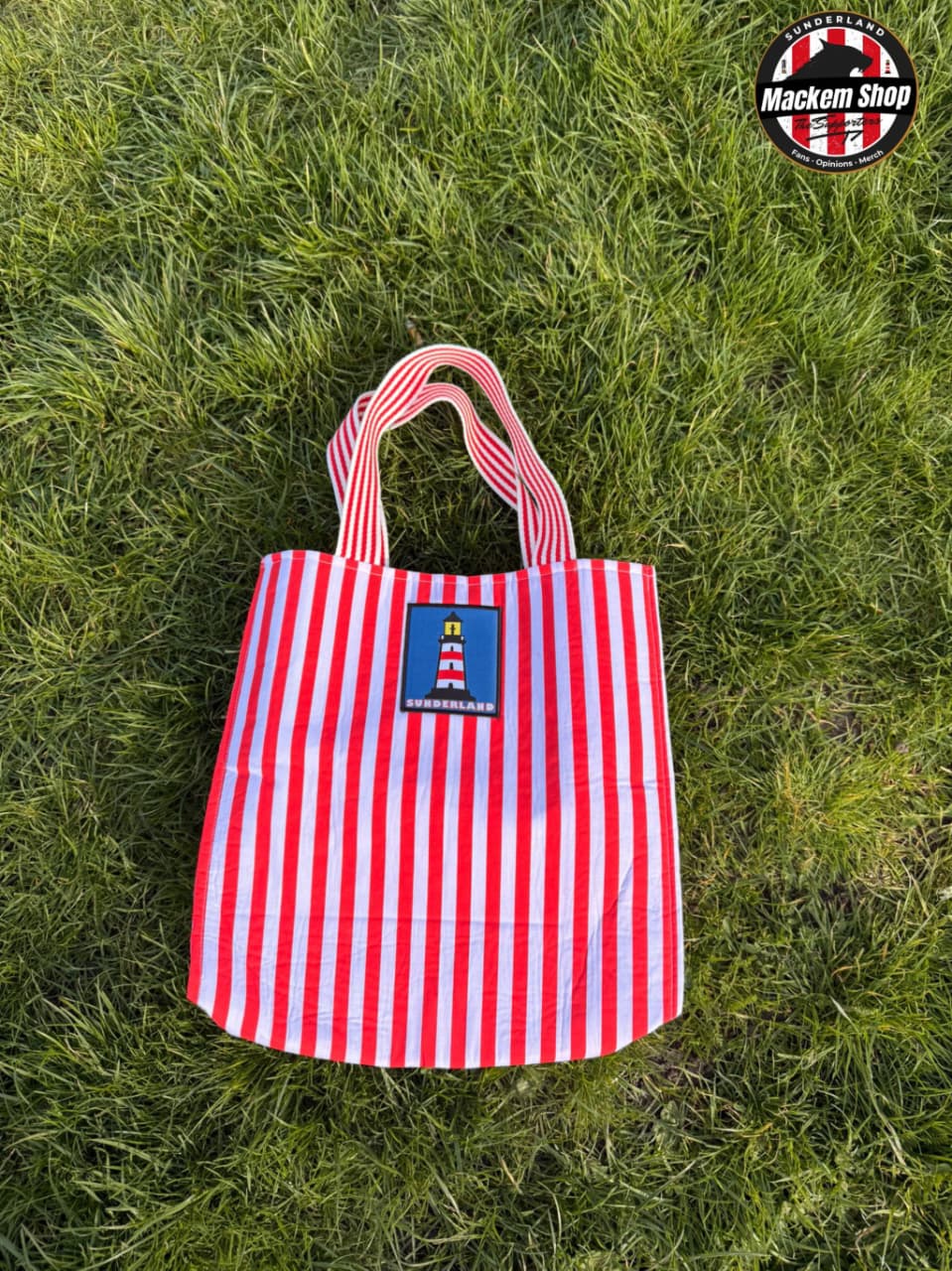 Red and white striped Tote bag with Sunderland Lighthouse logo put on grass, featuring 'Mackem Shop' logo.