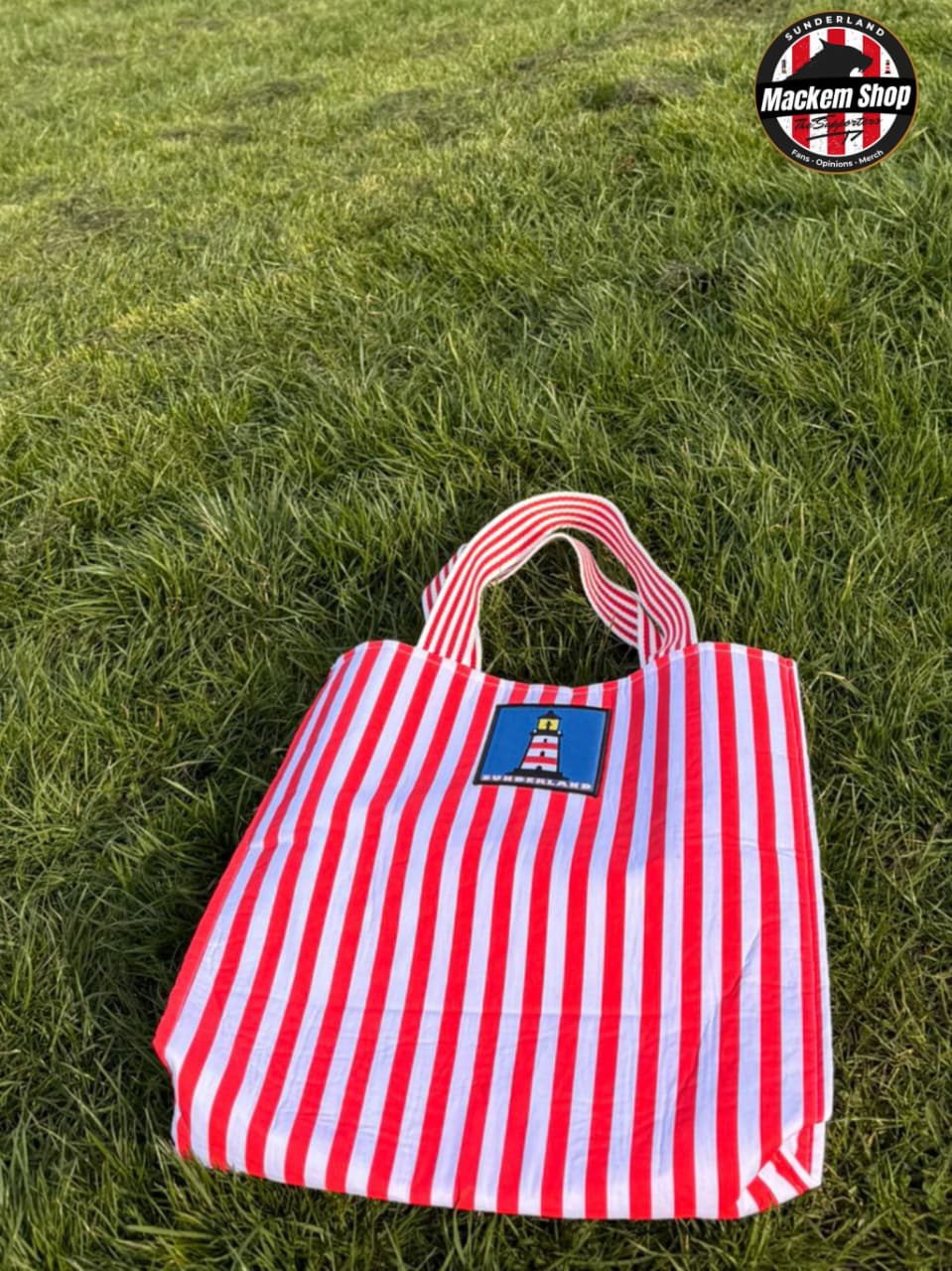 Red and white striped Tote bag with Sunderland Lighthouse logo put on grass, featuring 'Mackem Shop' logo.