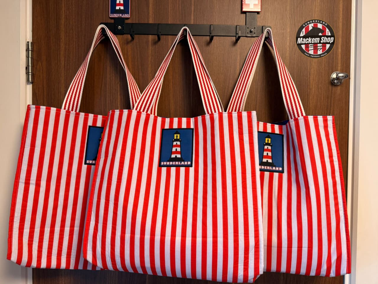 Multiple Sunderland tote bags hanging side by side showing front design and stripes