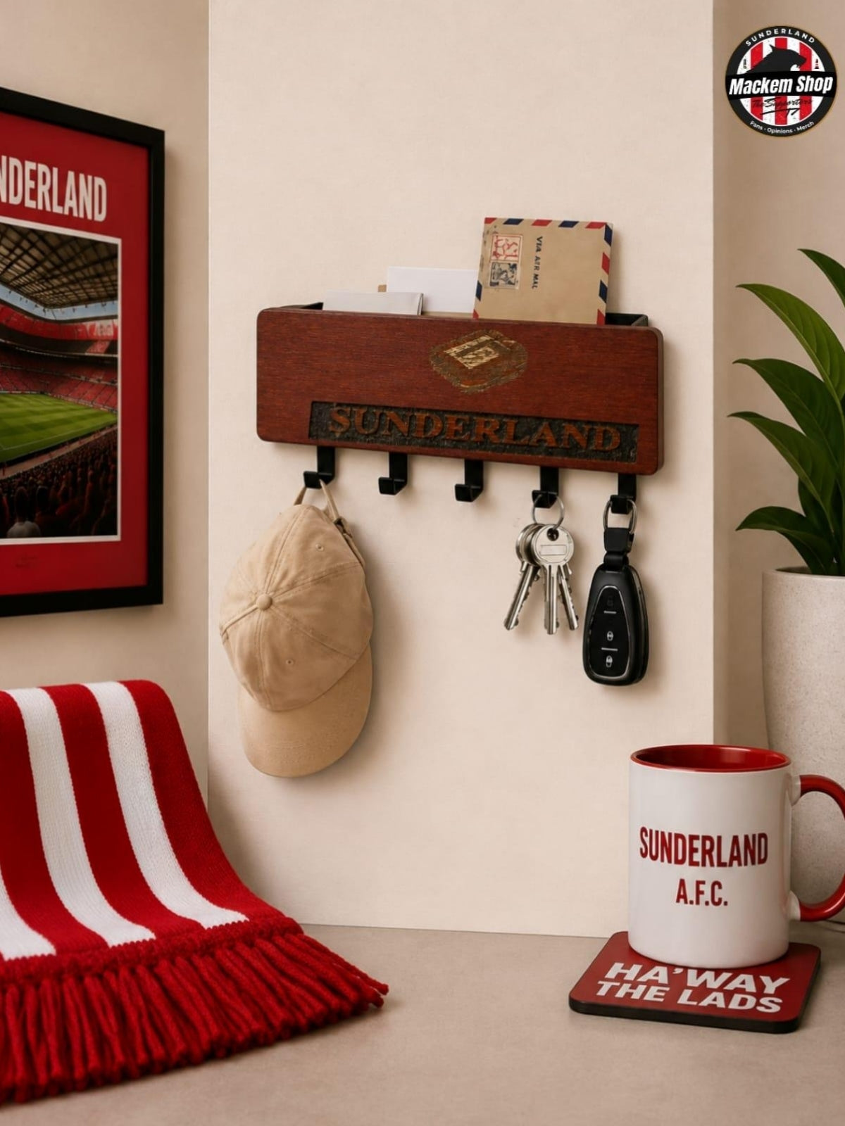 A wooden Sunderland AFC wall-mounted holder with black hooks, shown in a styled room setting with a red and white striped scarf, a framed stadium poster, keys, a beige cap, and a mug on a table.