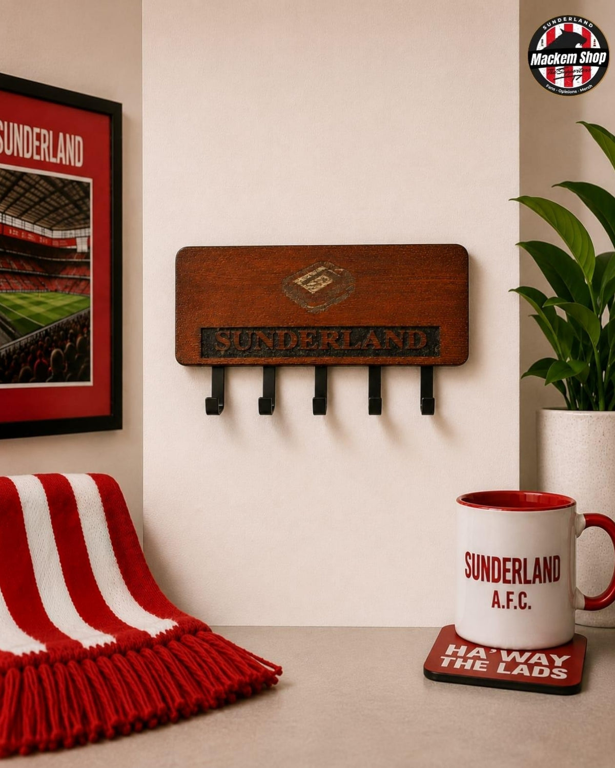 A wooden Sunderland AFC wall hook rack mounted on a beige wall, styled in a fan shop setting with a red and white striped scarf, a Sunderland mug, a plant, and a framed poster.