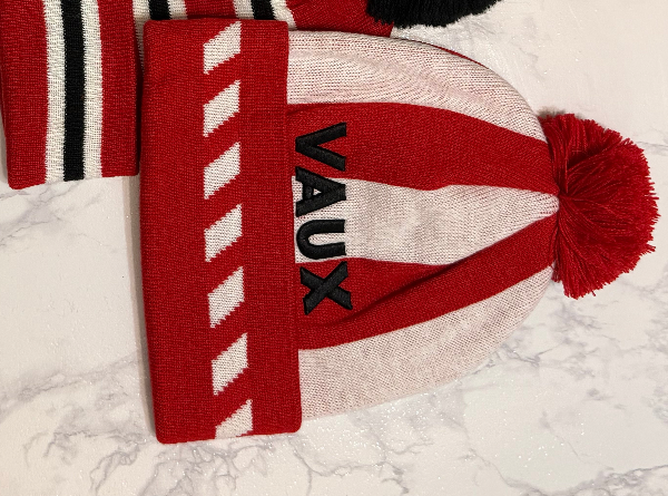 Red and white knit beanie with 'VAUX' branding on a marble surface
