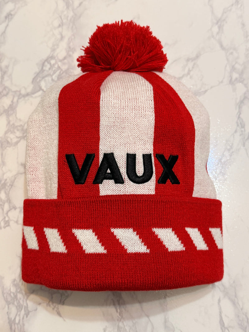 Red and white knitted hat with 'VAUX' branding on a marble surface