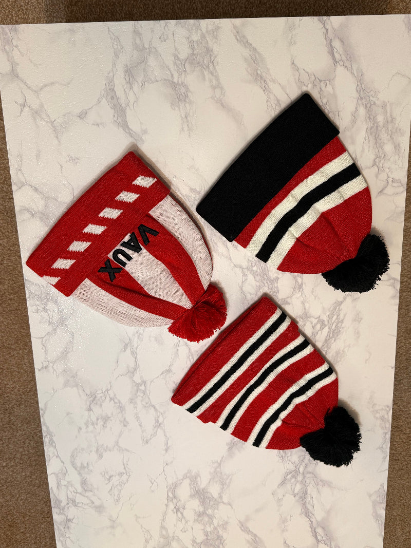 Three red and black beanies with pom-poms on a marble surface