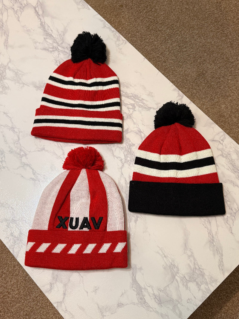Three red and black striped beanies with pom-poms on a marble surface