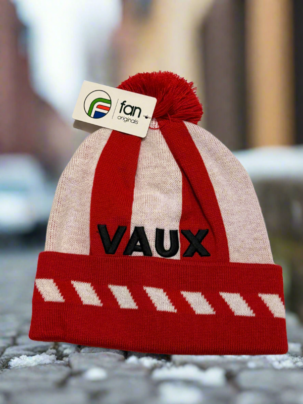 Red and beige beanie with 'VAUX' branding on a blurred street background