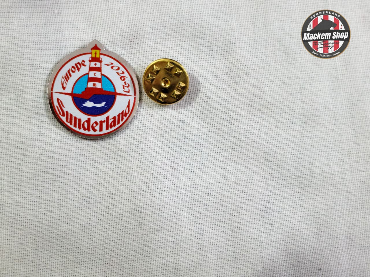 Two pins on a textured white background, one with a lighthouse design and text, the other gold.