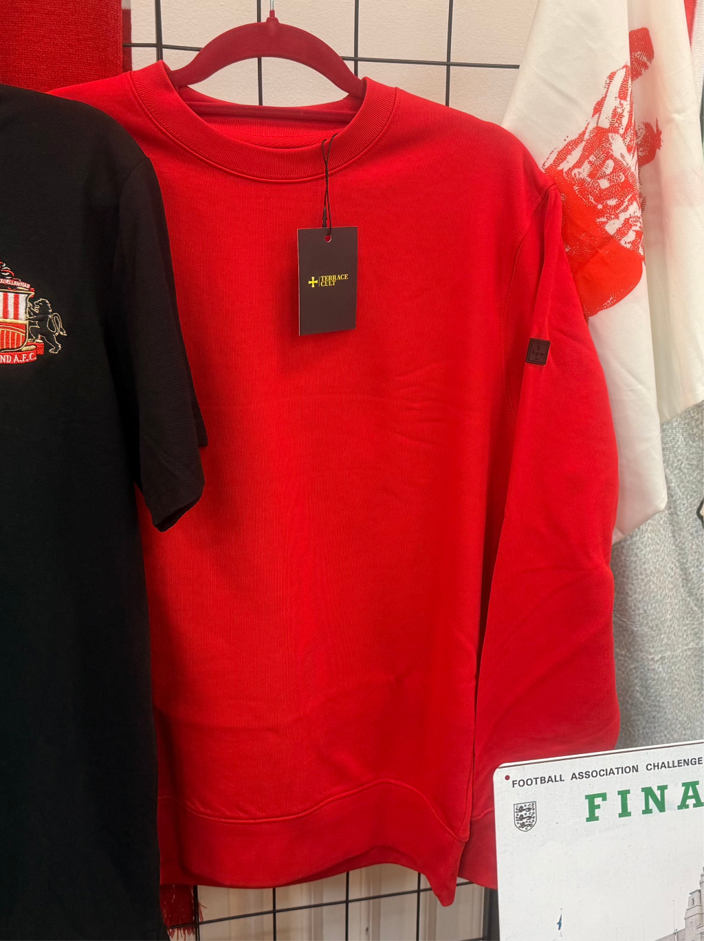 Red sweatshirt with a tag on a hanger against a tiled wall.