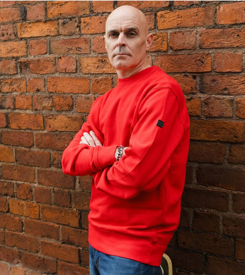 Man wearing a red sweatshirt against a brick wall