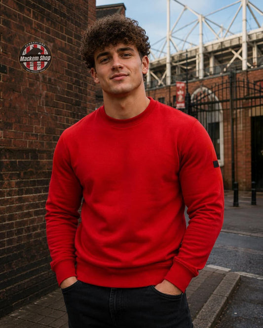 Man wearing a Red Terrace Cult Sweatshirt standing against a brick wall with a stadium in the background