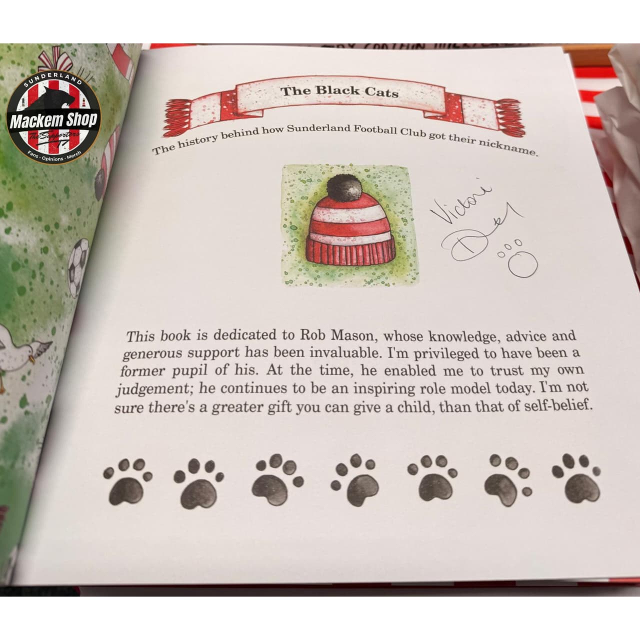 Book open to a page with text and illustrations, including a hat and paw prints, with 'Mackem Shop' logo on the top left corner.