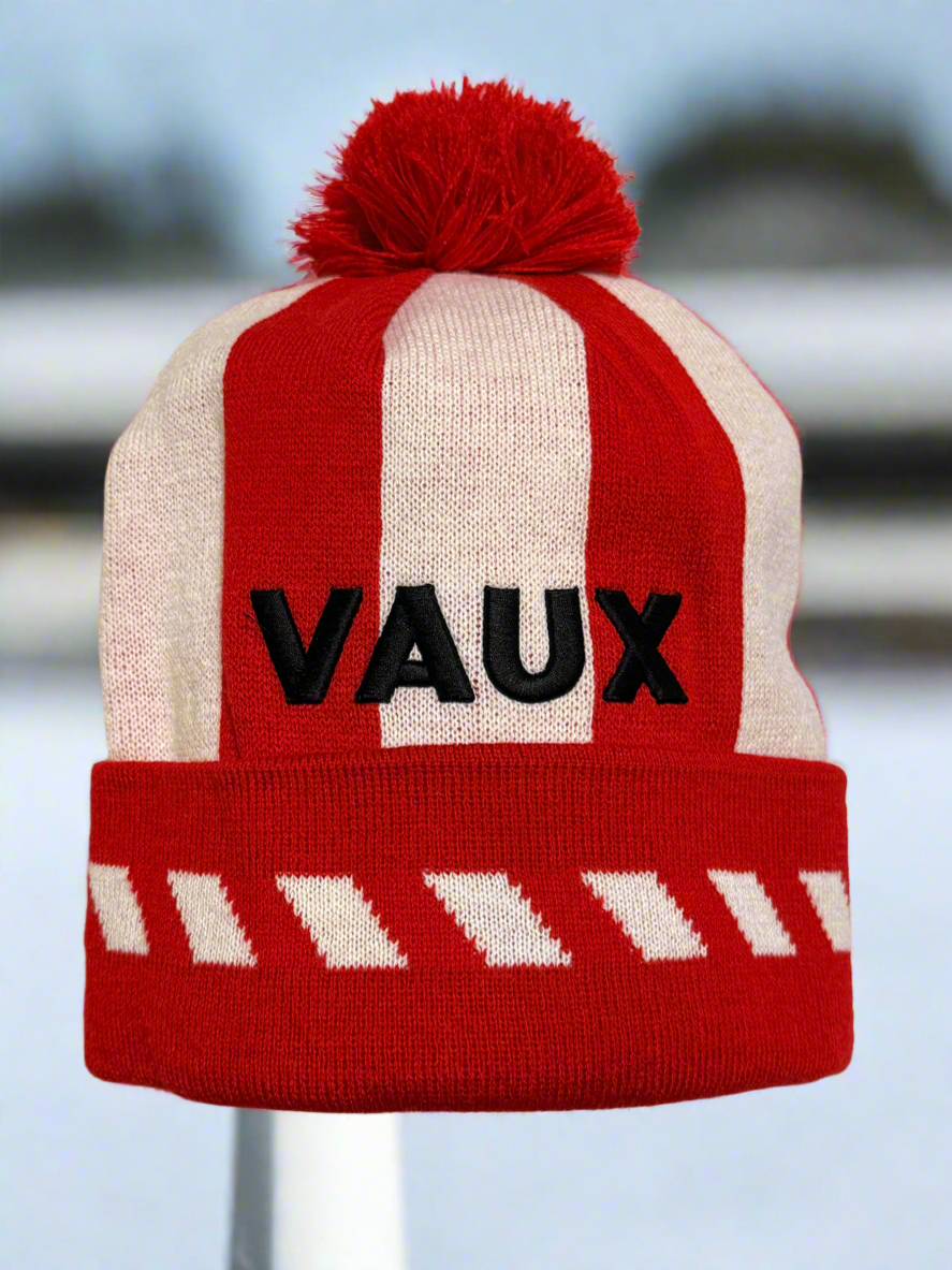 Red and white striped beanie with 'VAUX' branding on a blurred background