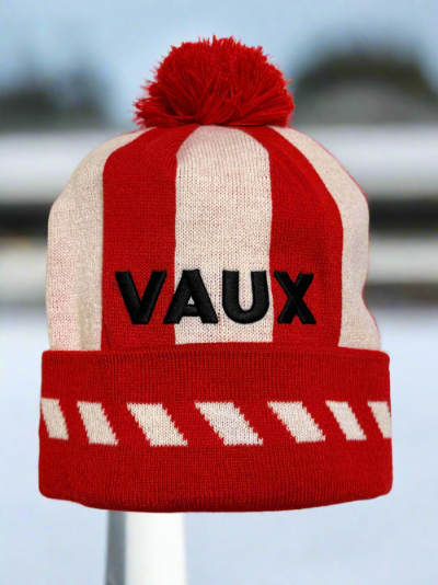 Red and white striped beanie with 'VAUX' branding on a blurred background