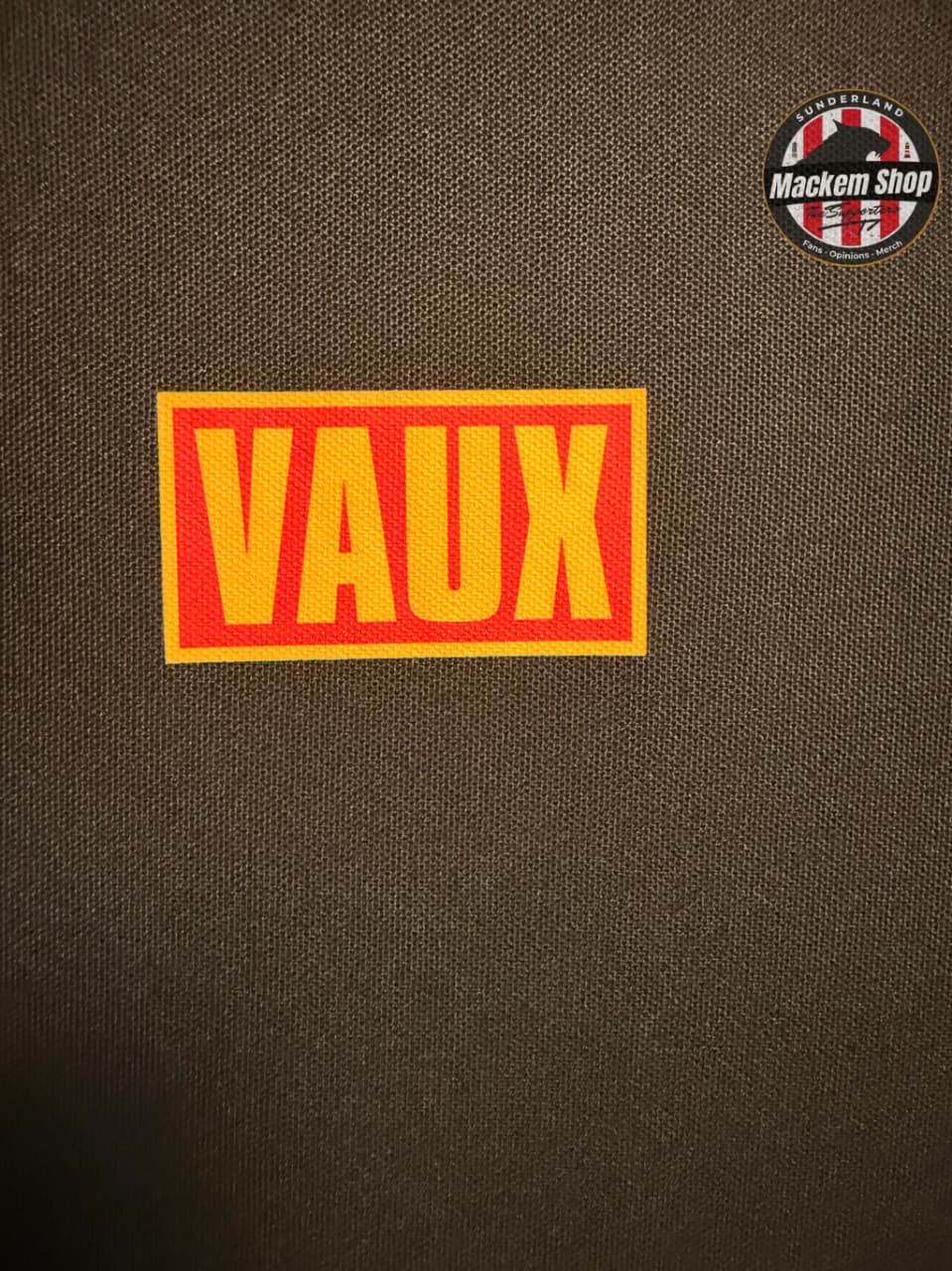 Red and yellow 'VAUX' patch on a black Polo shirt with Mackem Shop logo in the corner