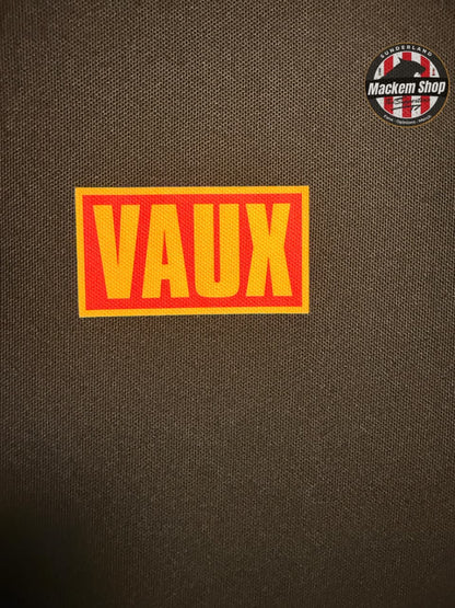 Red and yellow 'VAUX' patch on a black Polo shirt with Mackem Shop logo in the corner
