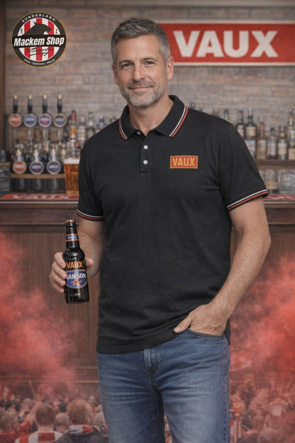 Man holding a Vaux beer bottle while wearing VAUX polo shirt in front of a bar with Vaux branding.