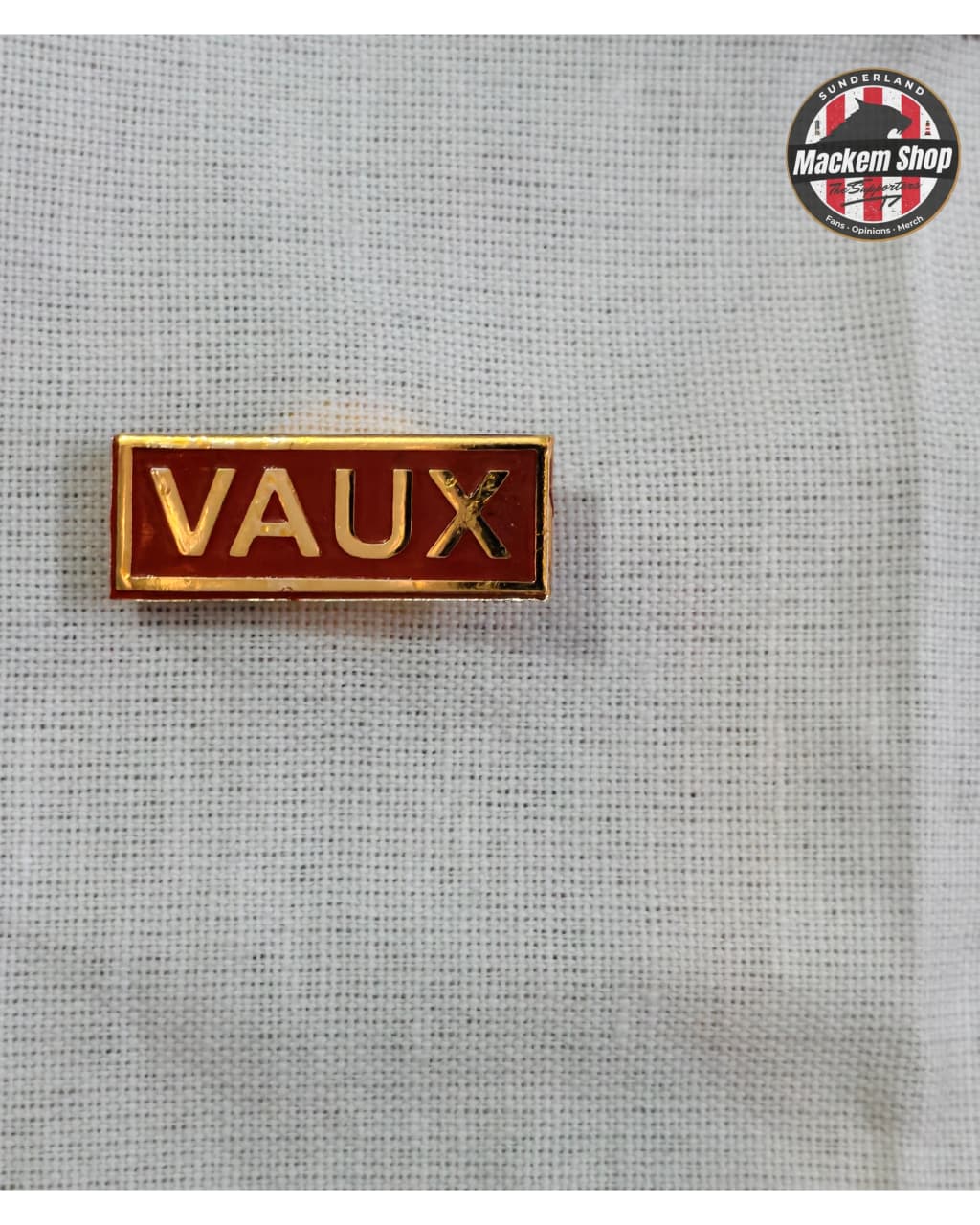 Pin with 'VAUX' text on a textured gray background