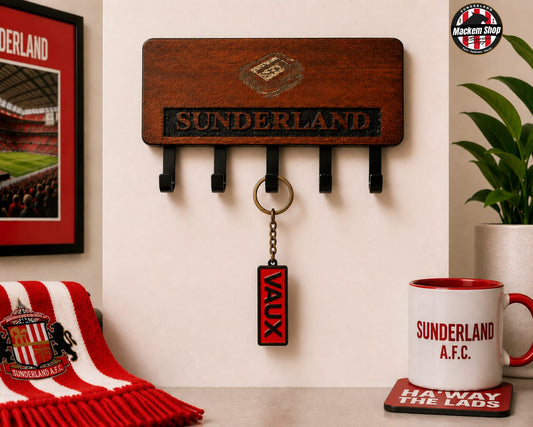 A wooden Sunderland AFC wall key holder with four black hooks, shown mounted on a beige wall in a styled room scene. A red and white Sunderland scarf is draped on the left, a framed Sunderland picture is partially visible, and a white Sunderland A.