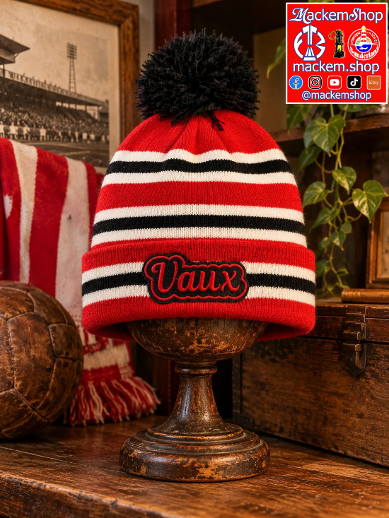 A red, black, and white striped knit beanie with a black pom-pom on top, displayed on a rustic wooden pedestal. The front of the beanie features an embroidered patch reading 'Vaux' in black with a red outline. A MackemShop Logo is visible on top right corner.