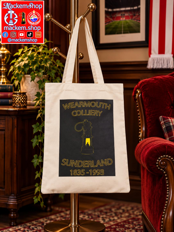 A tote bag hanging on a brass coat rack in a vintage-style room. The tote bag is off-white with a large black graphic panel featuring gold text that reads 'WEARMOUTH COLLIERY' and 'SUNDERLAND 1835-1993' with a lantern illustration. A MackemShop Logo is visible on top left corner.