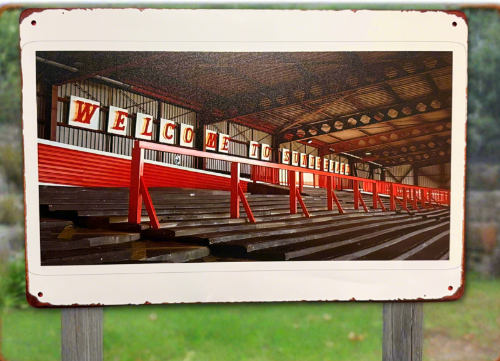 Metal sign with a photo of an indoor arena and 'Welcome to Evergreen' sign.