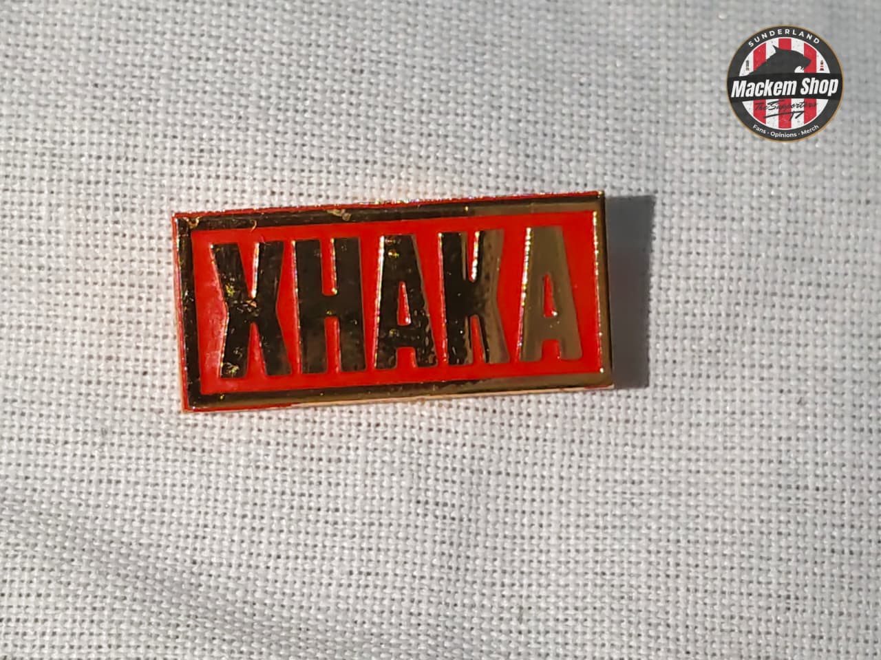Red and gold 'Xhaka' badge on a textured gray background with 'MackemShop' logo.