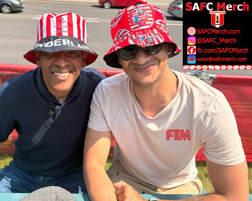 Two men wearing colorful hats sitting on a grassy area with promotional text for SAFC Merch overlayed.
