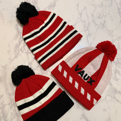 Three red beanies with pom-poms on a marble surface